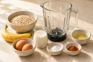 Rolled oats, ripe banana, two eggs and milk beside a blender