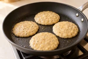 Small banana oat pancakes with bubbles forming in a skillet