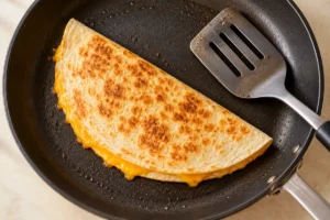 A folded quesadilla browning in a skillet with a broad spatula